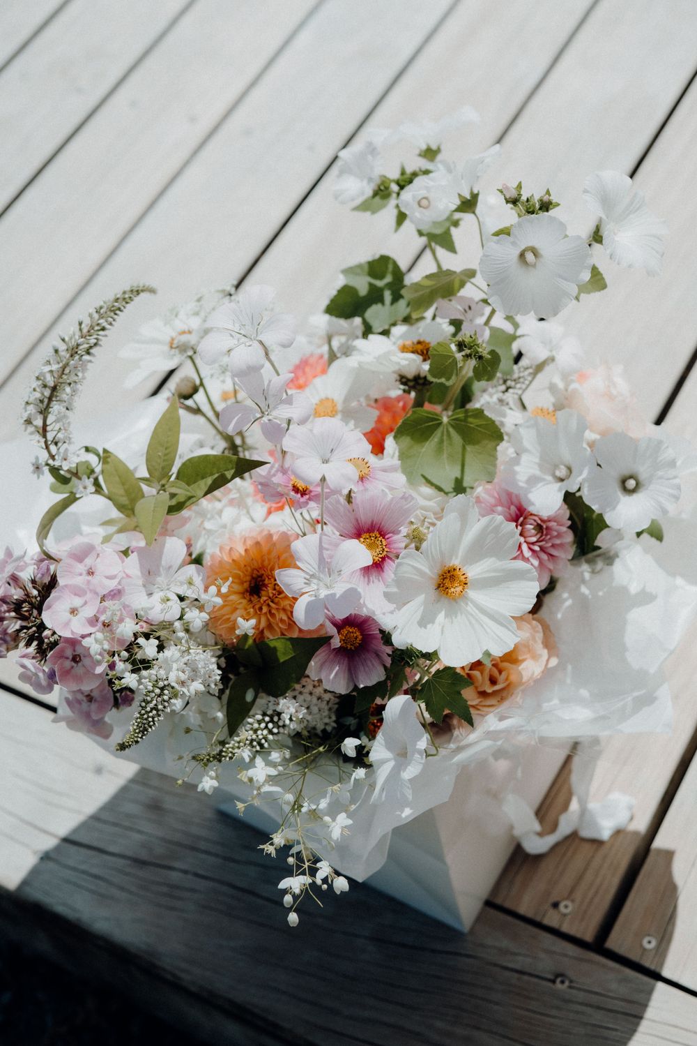 Beautiful floral arrangement with white and peach blooms on wooden deck.