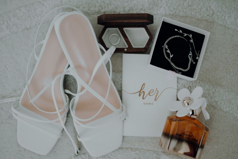 Elegant bridal accessories including white sandals, perfume bottle and wedding stationery.