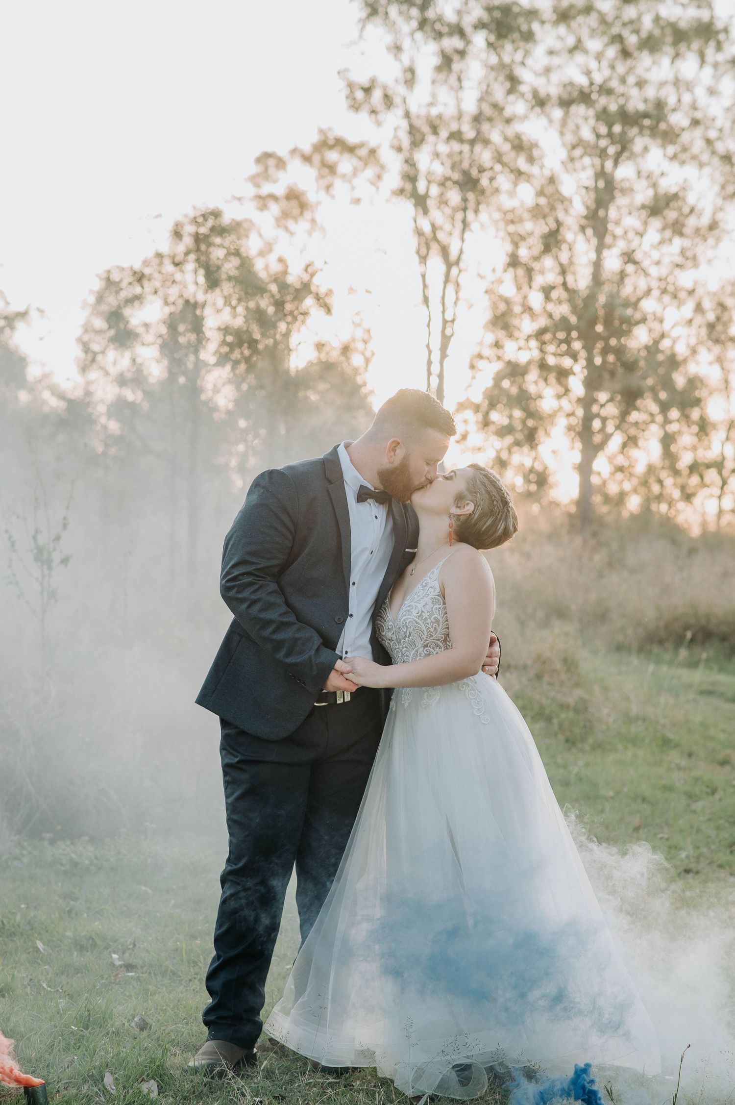 Romantic wedding portrait with smoke effect in misty outdoor setting.