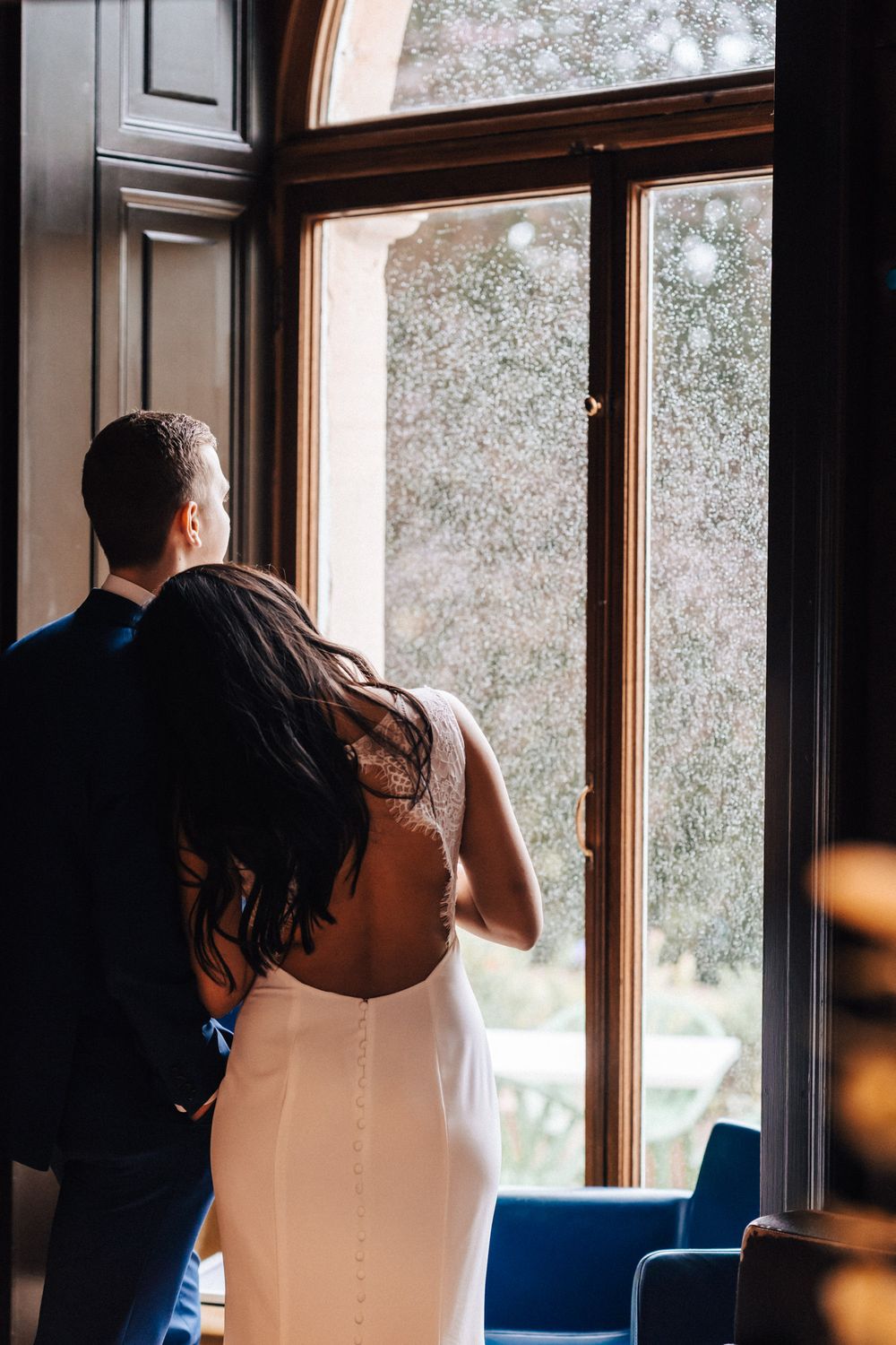 Bride and groom looking out of the window at Cowley Manor cuddling warm loving photograph