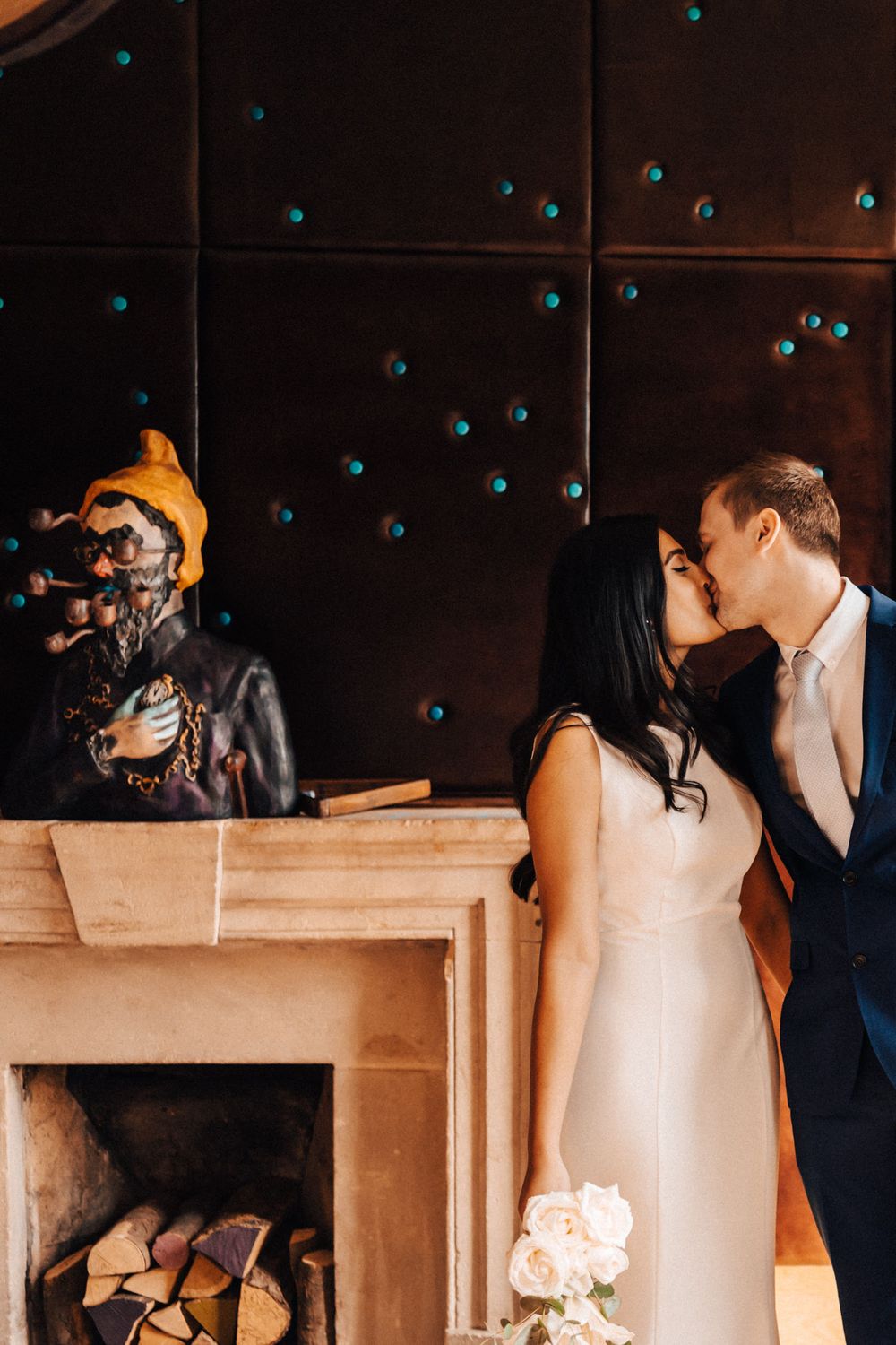 Bride and groom kissing by the fireplace at Cowley Manor