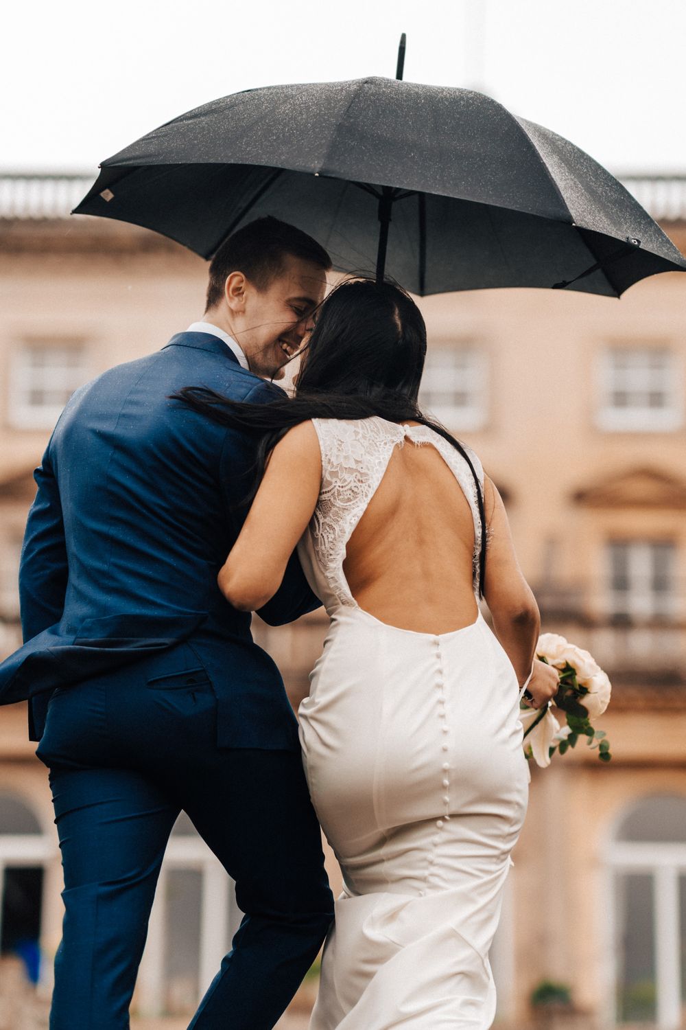 Bride and groom with and umbrella on the stairs outside kissing