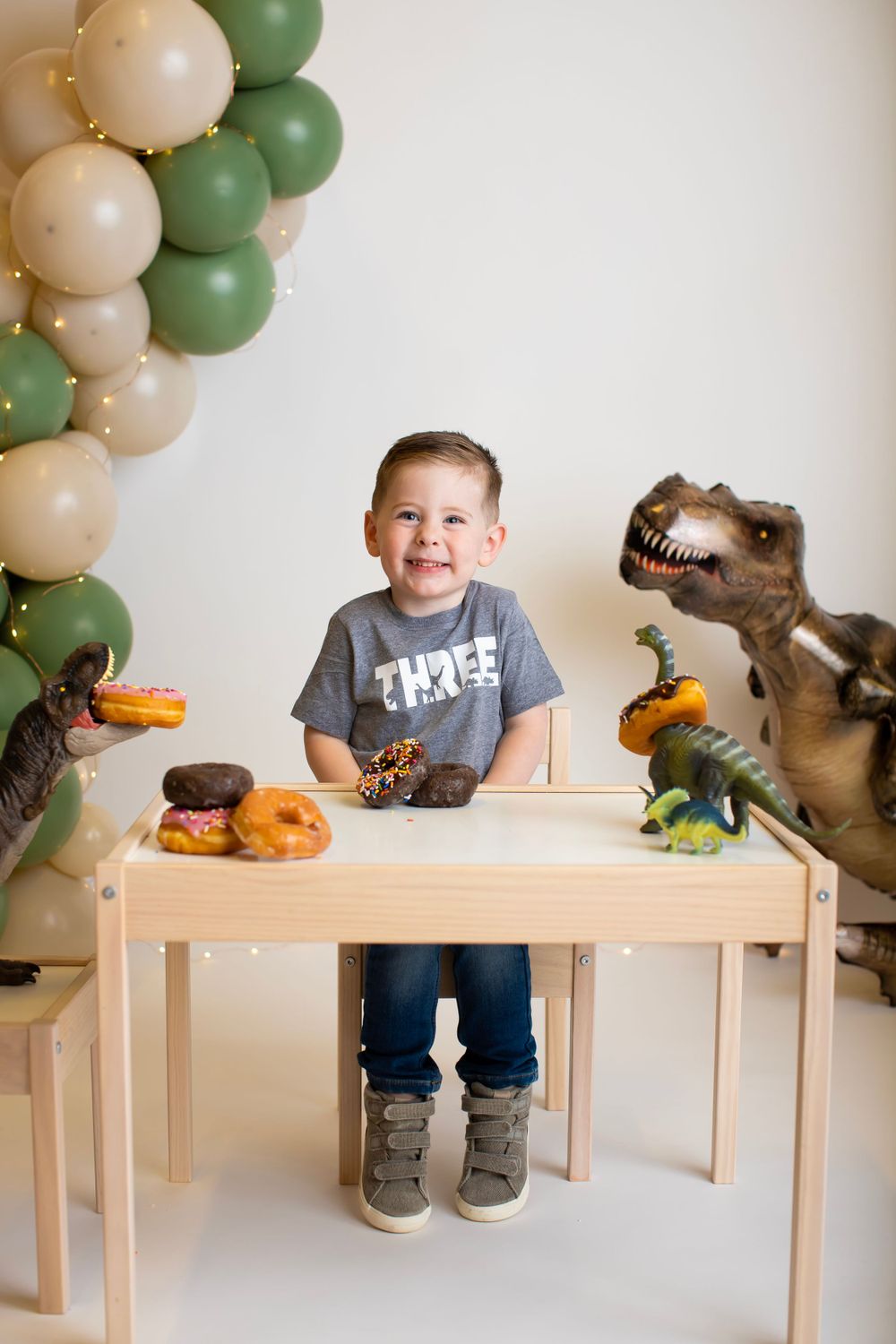 Child celebrates with toy dinosaurs and treats at decorated birthday table.