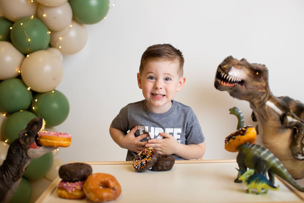 Playful birthday scene with toy dinosaurs and donuts surrounded by festive balloons.