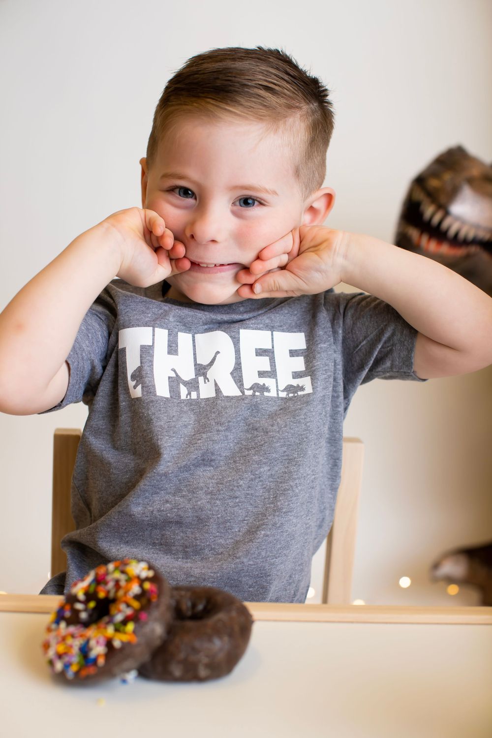Playful portrait with donuts and grey t-shirt against white background.
