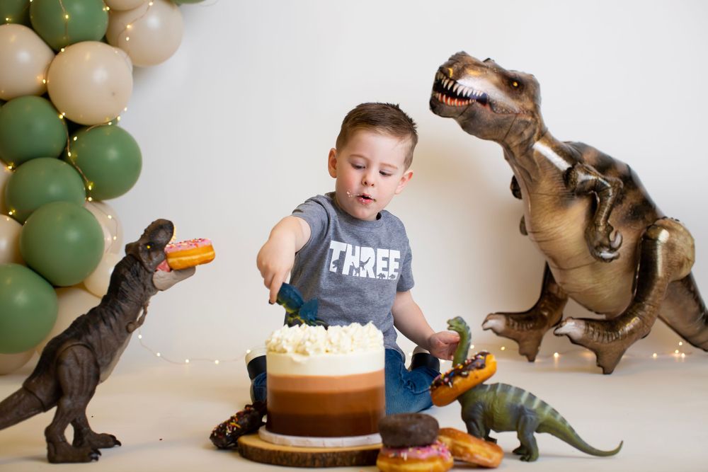 Birthday cake and donuts surrounded by playful dinosaur decorations and balloon arch.