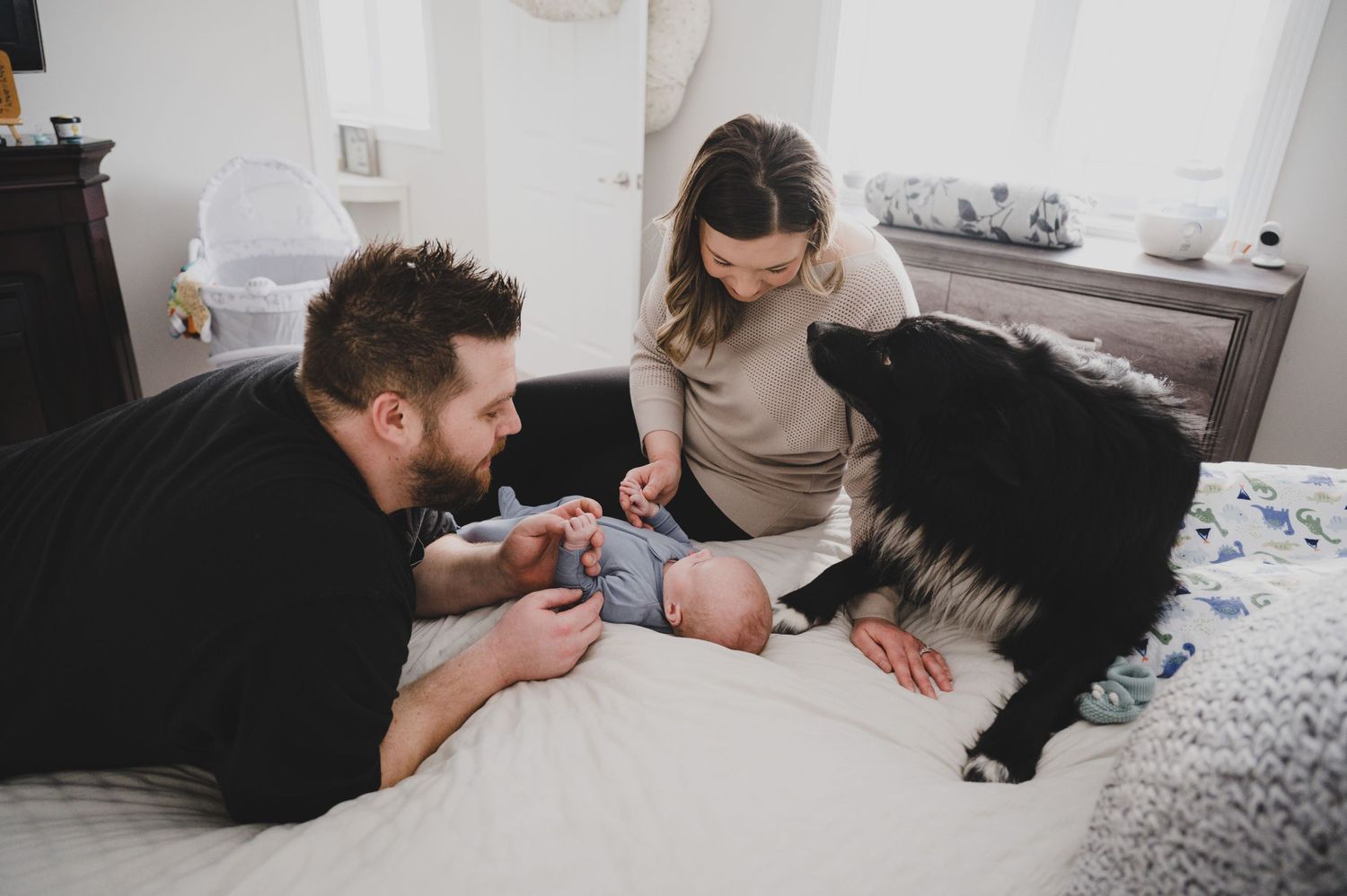 Parents playing with baby on bed while black cat watches nearby.