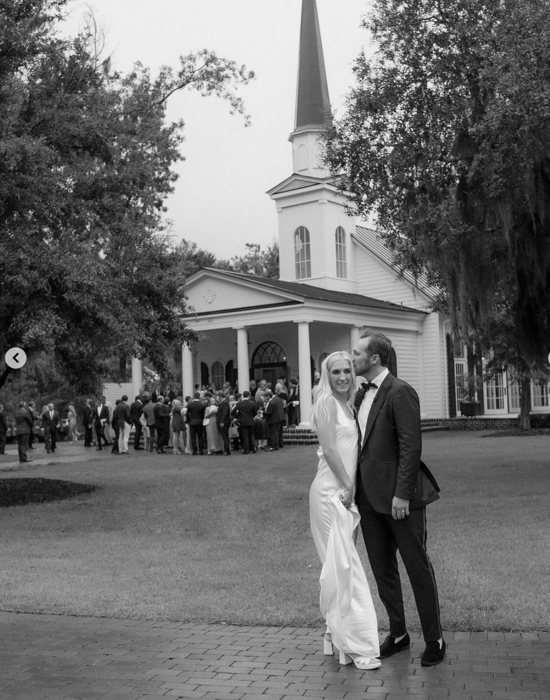 Classic black and white wedding photo outside white church with gathering crowd.