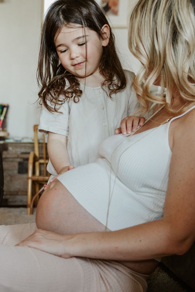 petite fille caresse le ventre de sa maman enceinte pendant un shooting photo grossesse en famille à à domicile Lille