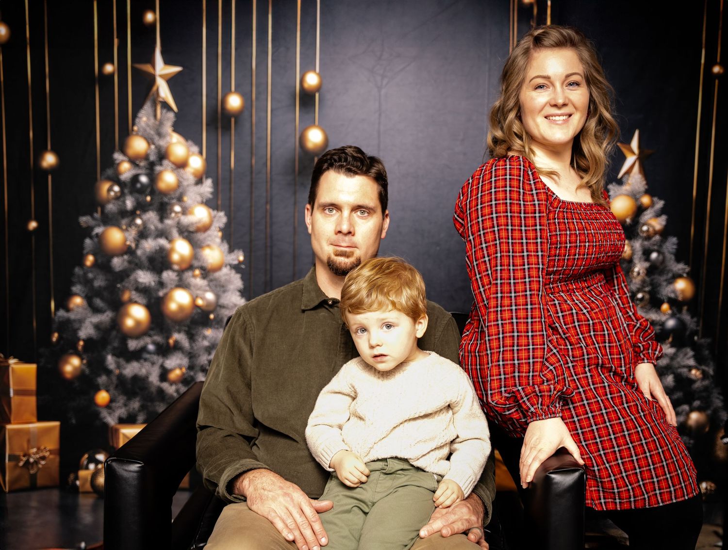 A family holiday portrait with decorated Christmas trees and hanging lights in the background.