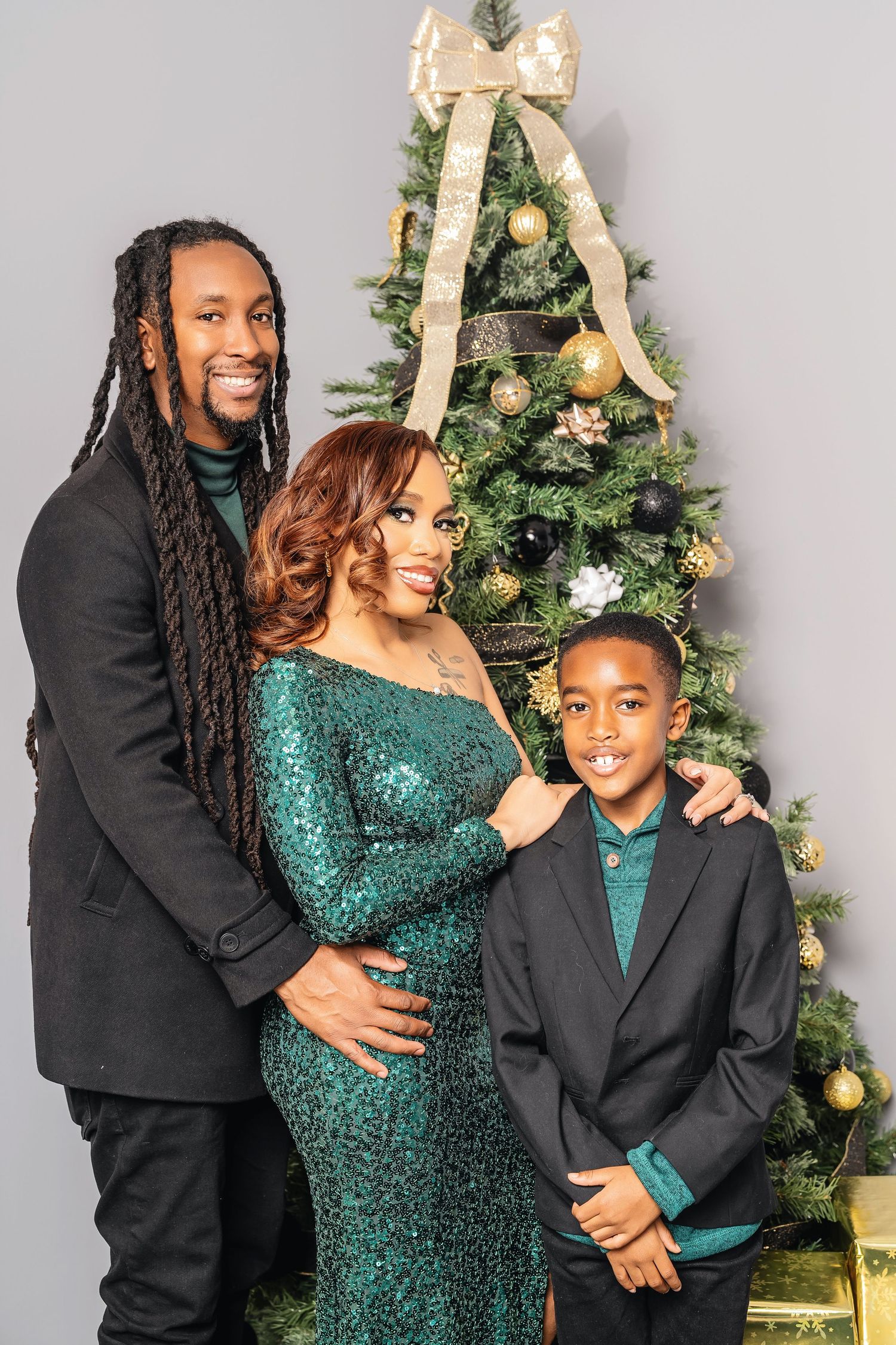 Family poses in elegant attire by a decorated Christmas tree with a large gold bow.