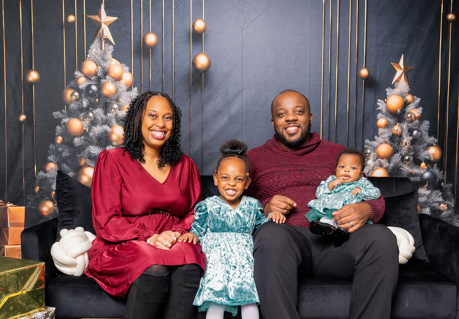 Holiday family portrait with Christmas trees and golden decorations in the background.