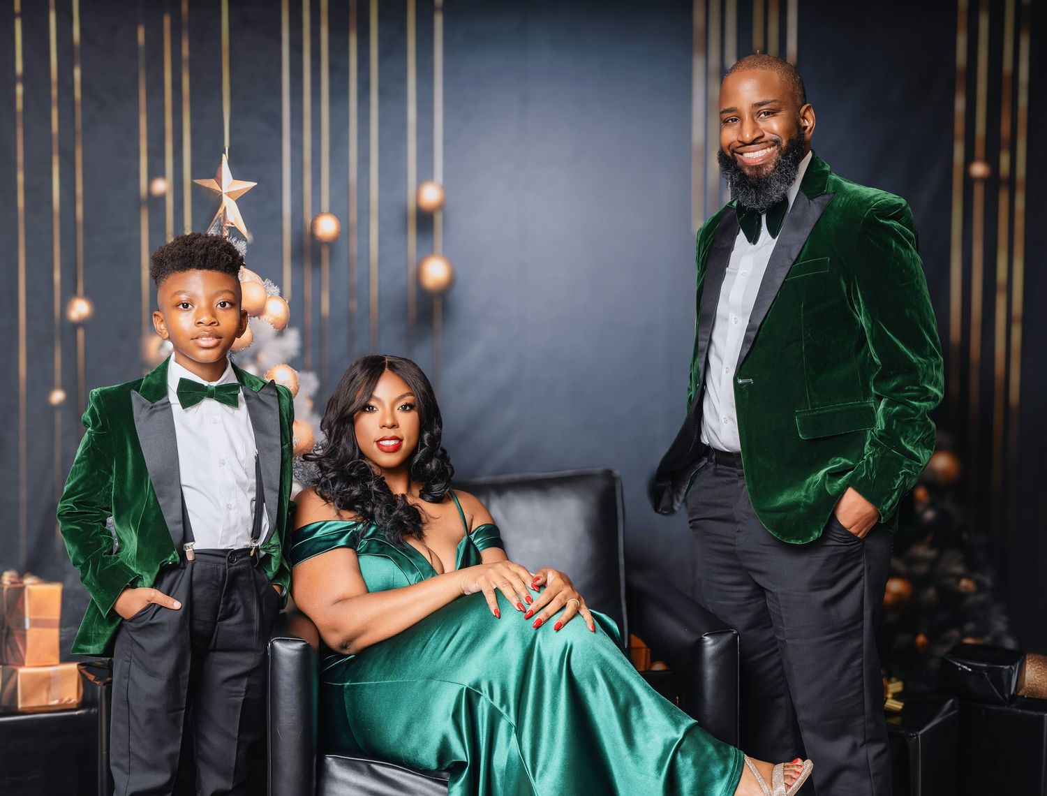 Family in coordinating green velvet and silk formal attire poses together against a dark backdrop with gold decor.