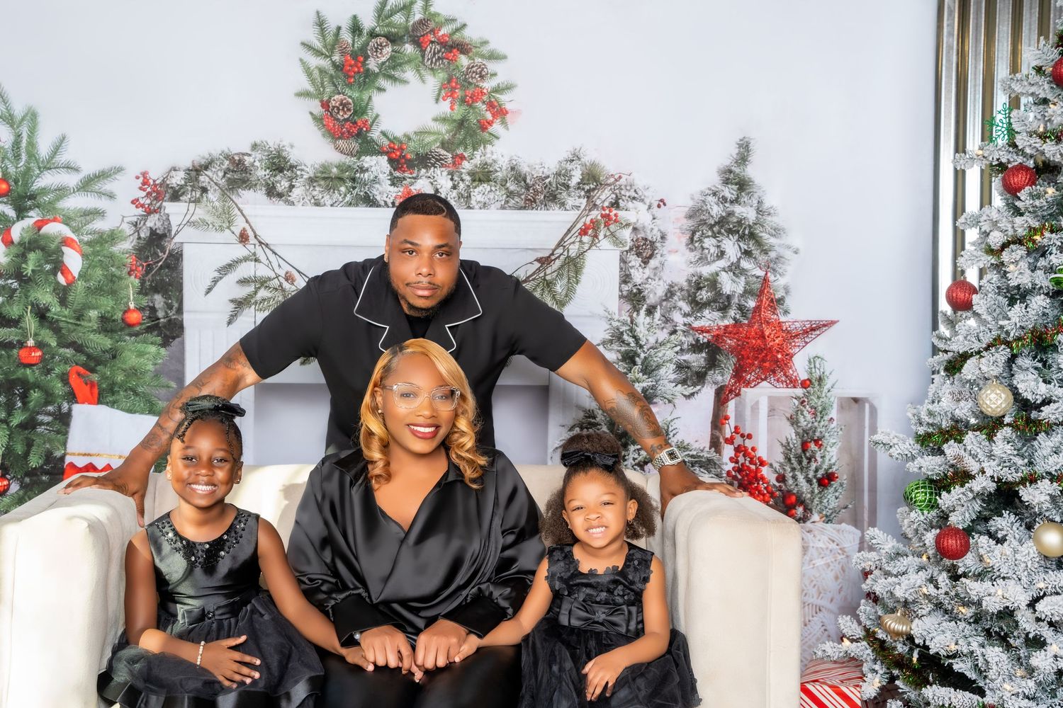 A festive family photo taken in front of decorated Christmas trees and wreaths in a cozy holiday setting.