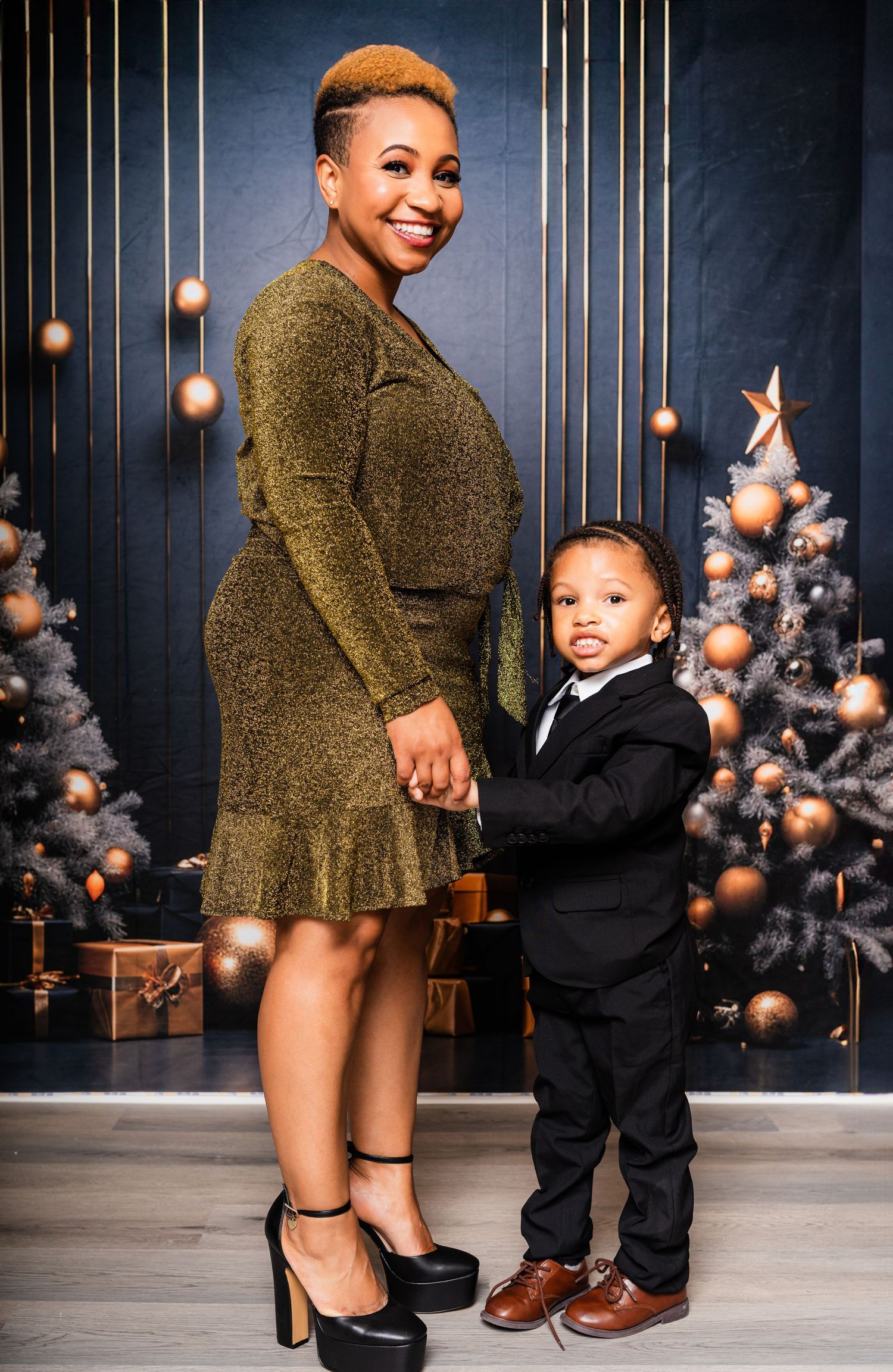A holiday portrait with decorative trees showing a woman in gold dress posing with child in formal attire.