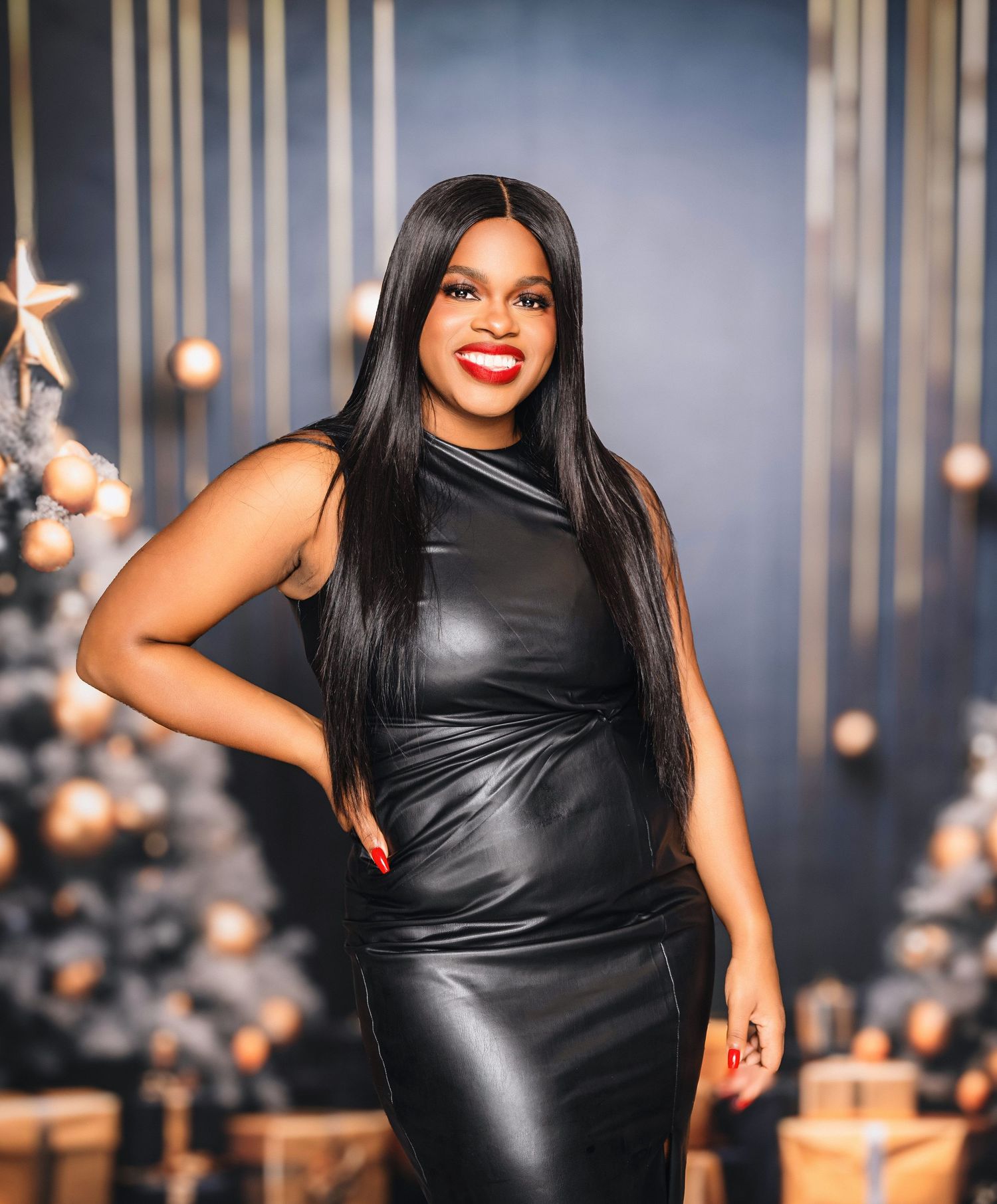 A confident person poses in a sleek black leather dress against a festive background with Christmas decorations.