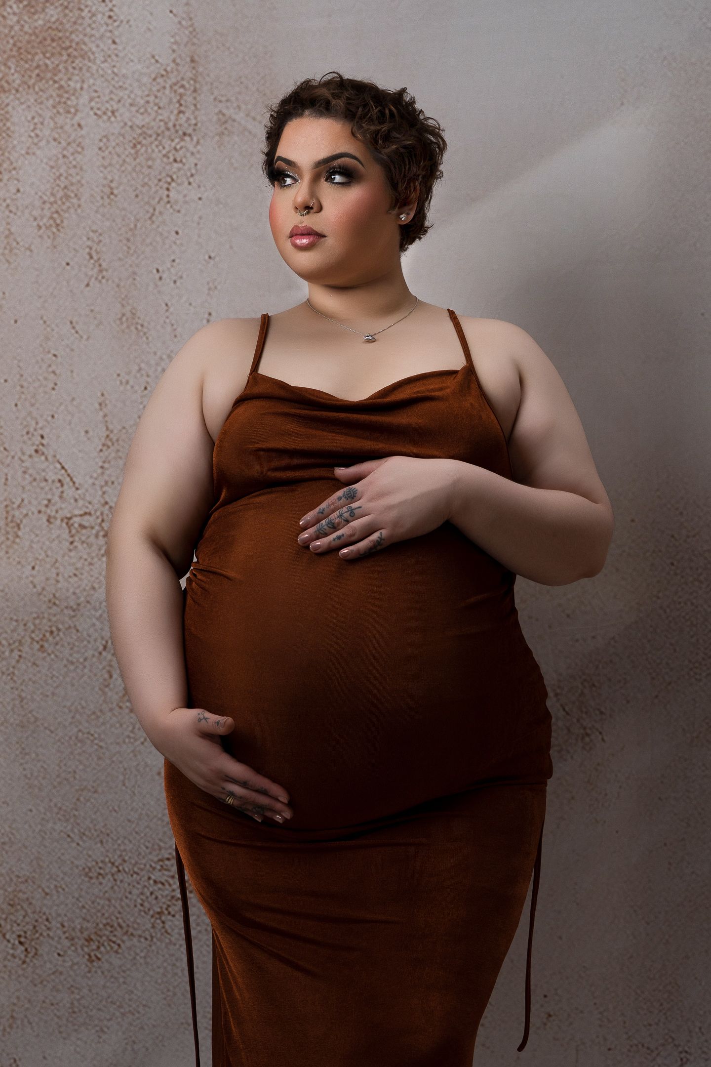 Mother to be with short hair in a brown gown with a textured backdrop in studio.
