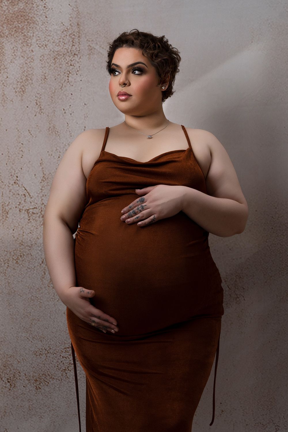 Mother to be with short hair in a brown gown with a textured backdrop in studio.