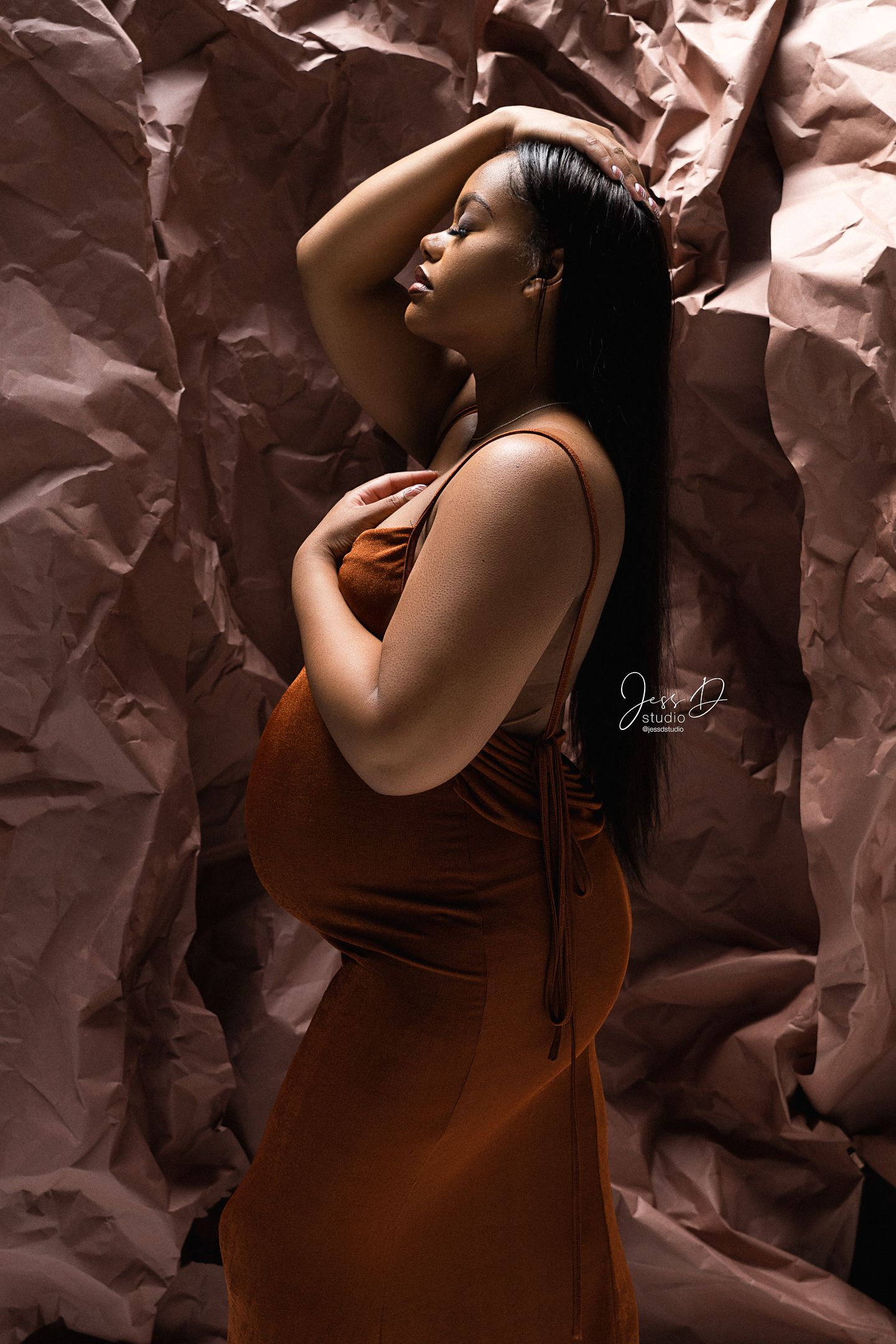 Mother to be in a brown gown with a textured backdrop that resembles rocks in studio.