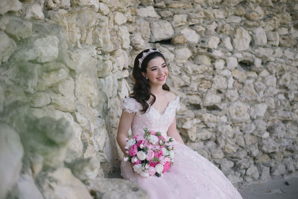 Bride holding pink and white bouquet poses against weathered stone wall backdrop.