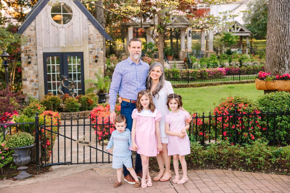 A family stands together in front of a charming garden cottage with autumn decorations.