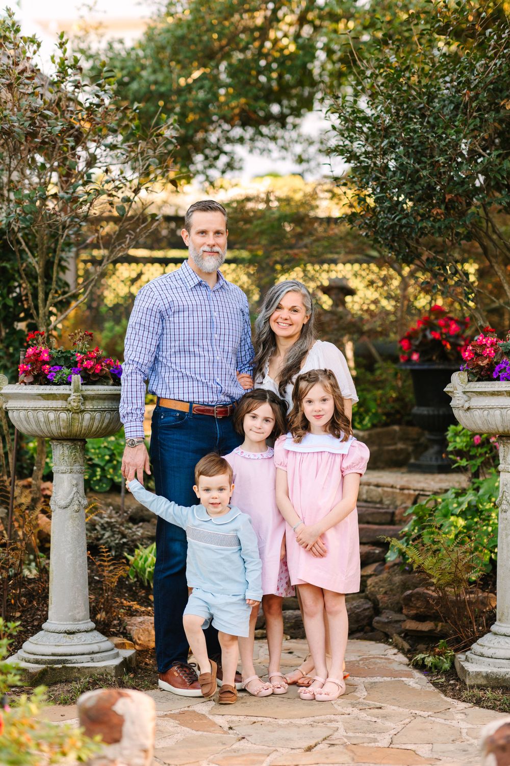 A family portrait taken in a garden setting with stone pillars and colorful flowers in the background.