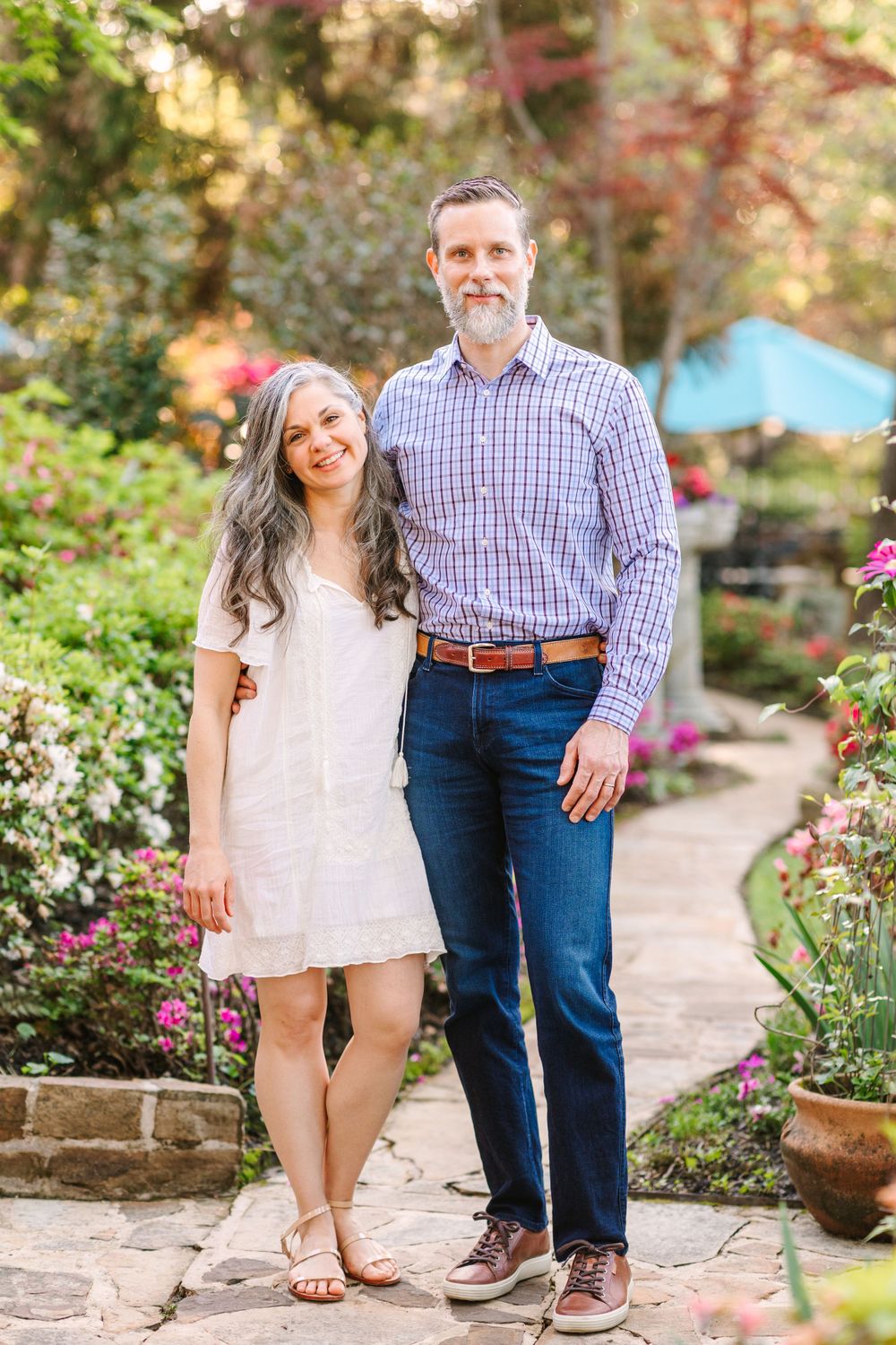 A couple stands together on a stone pathway surrounded by beautiful garden landscaping and fall foliage.