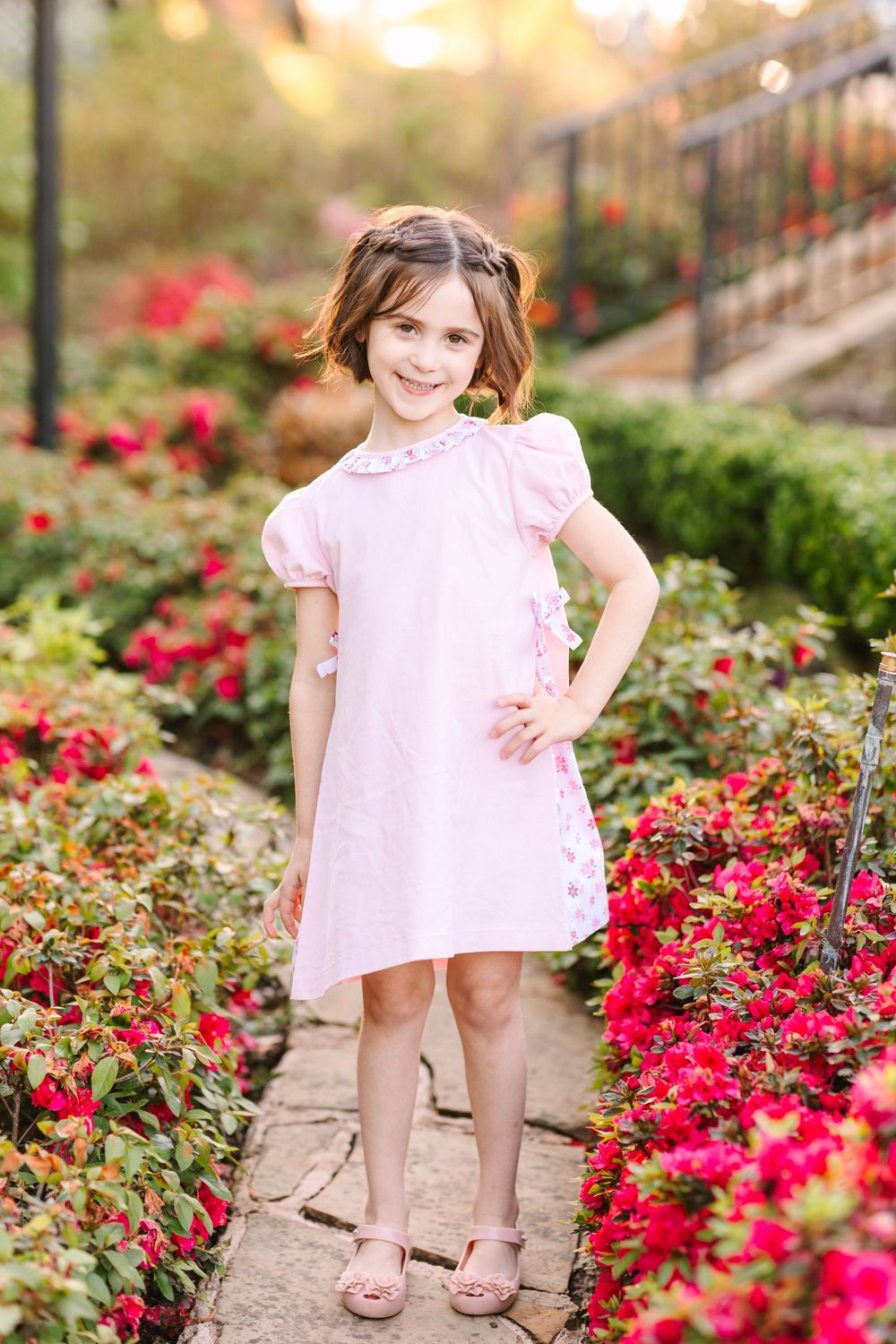 Child in pink dress standing on stone path surrounded by vibrant red flowers.