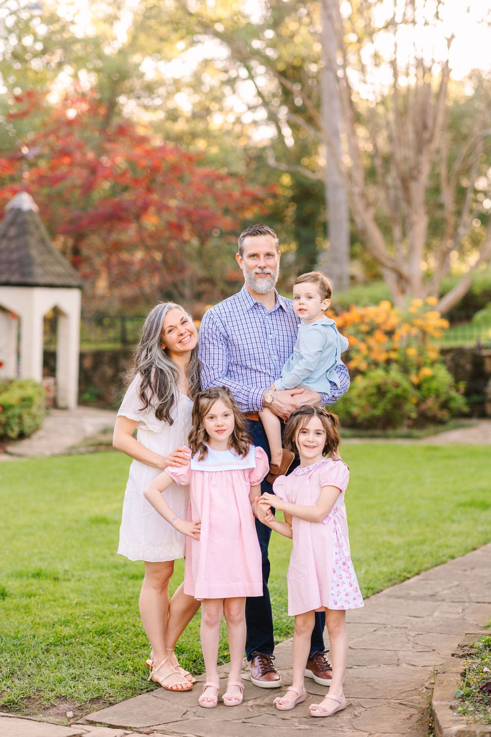 A family of five poses together on a garden path with fall foliage and landscaping in the background.