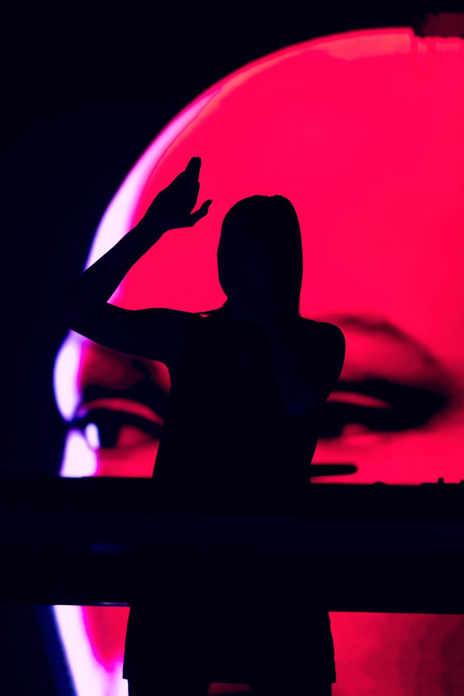 Dramatic silhouette of performer against large red circular lighting display.