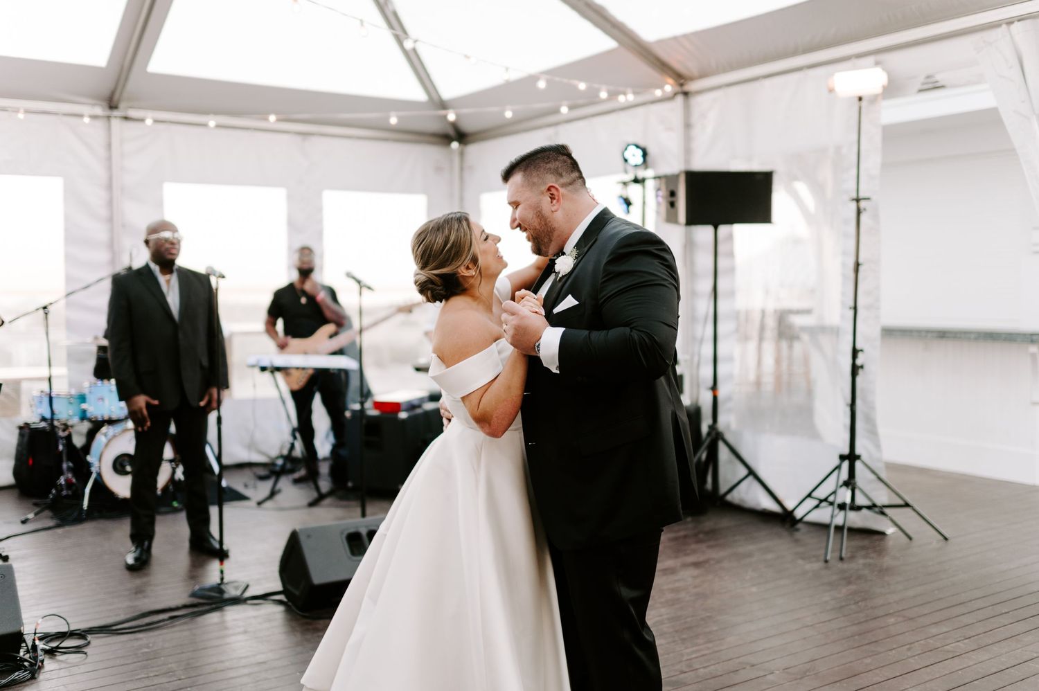 Wedding couple shares romantic dance moves under white tent with reception setup visible.