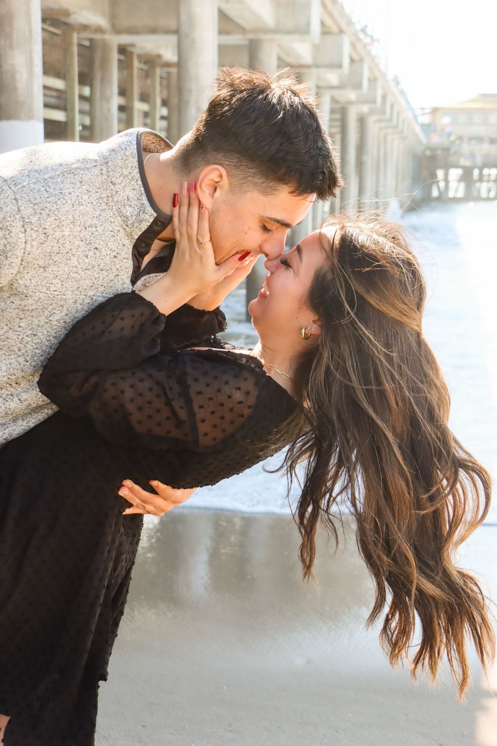 Romantic beach portraits captured under pier with dramatic lighting.