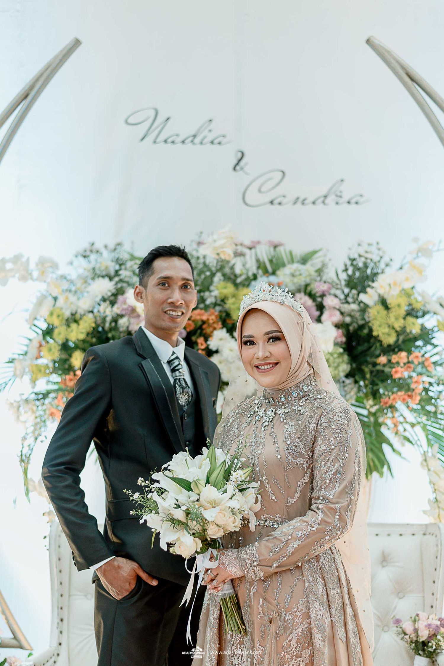 Wedding portrait featuring formal attire against a white floral arch backdrop.