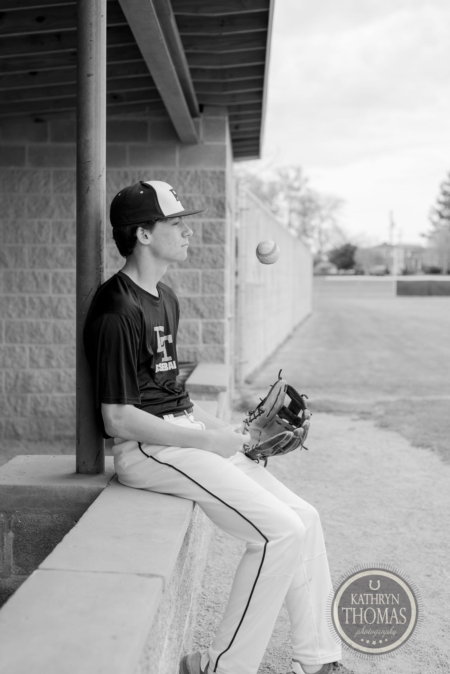 Baseball player in dugout wearing cap and uniform in black and white photograph.