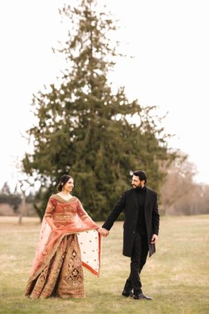 A couple in traditional attire walks hand in hand across a grassy field.