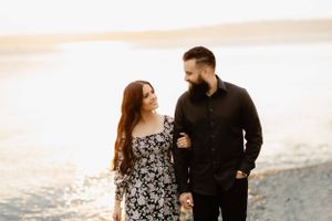 Couple walking together along shoreline at sunset.