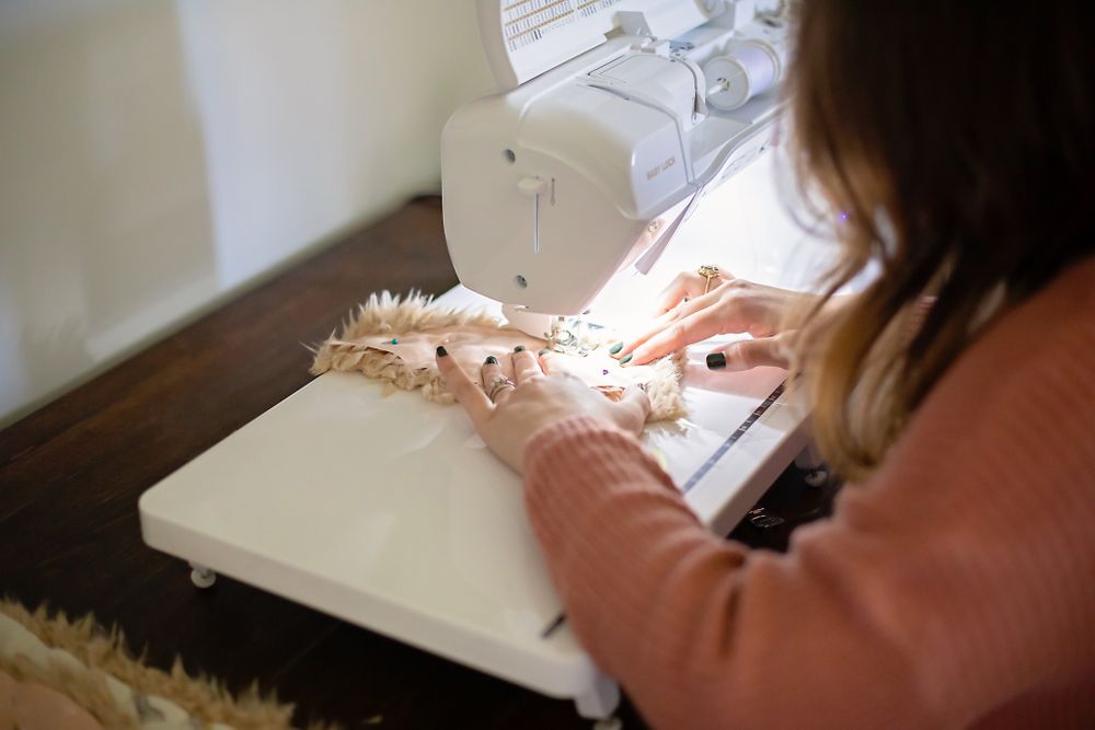 Hands operating sewing machine with fabric on white surface.