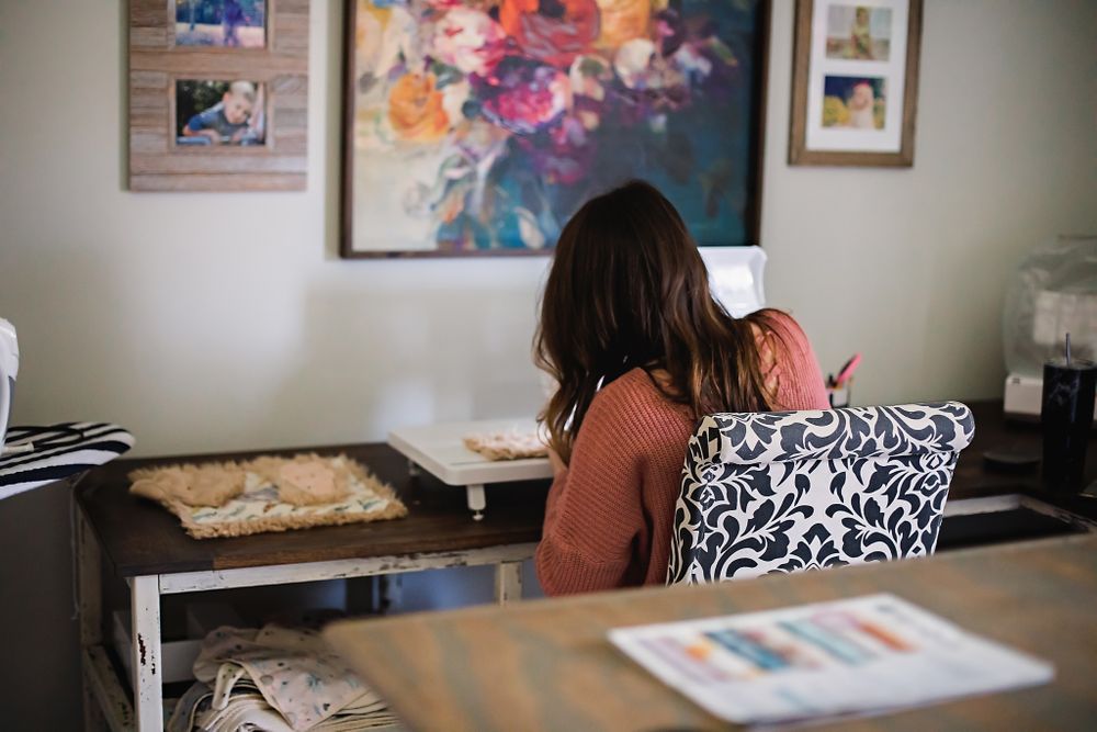 Back view of person at desk with sewing machine and black and white patterned pillow.