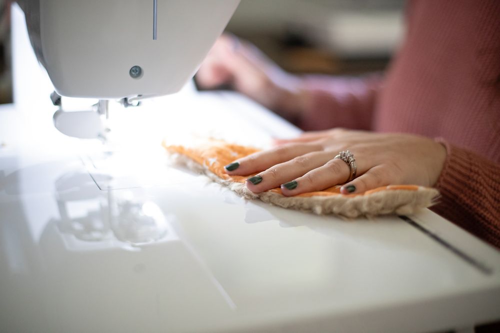 Close-up of hands using a sewing machine with peach colored fabric and diamond ring visible.