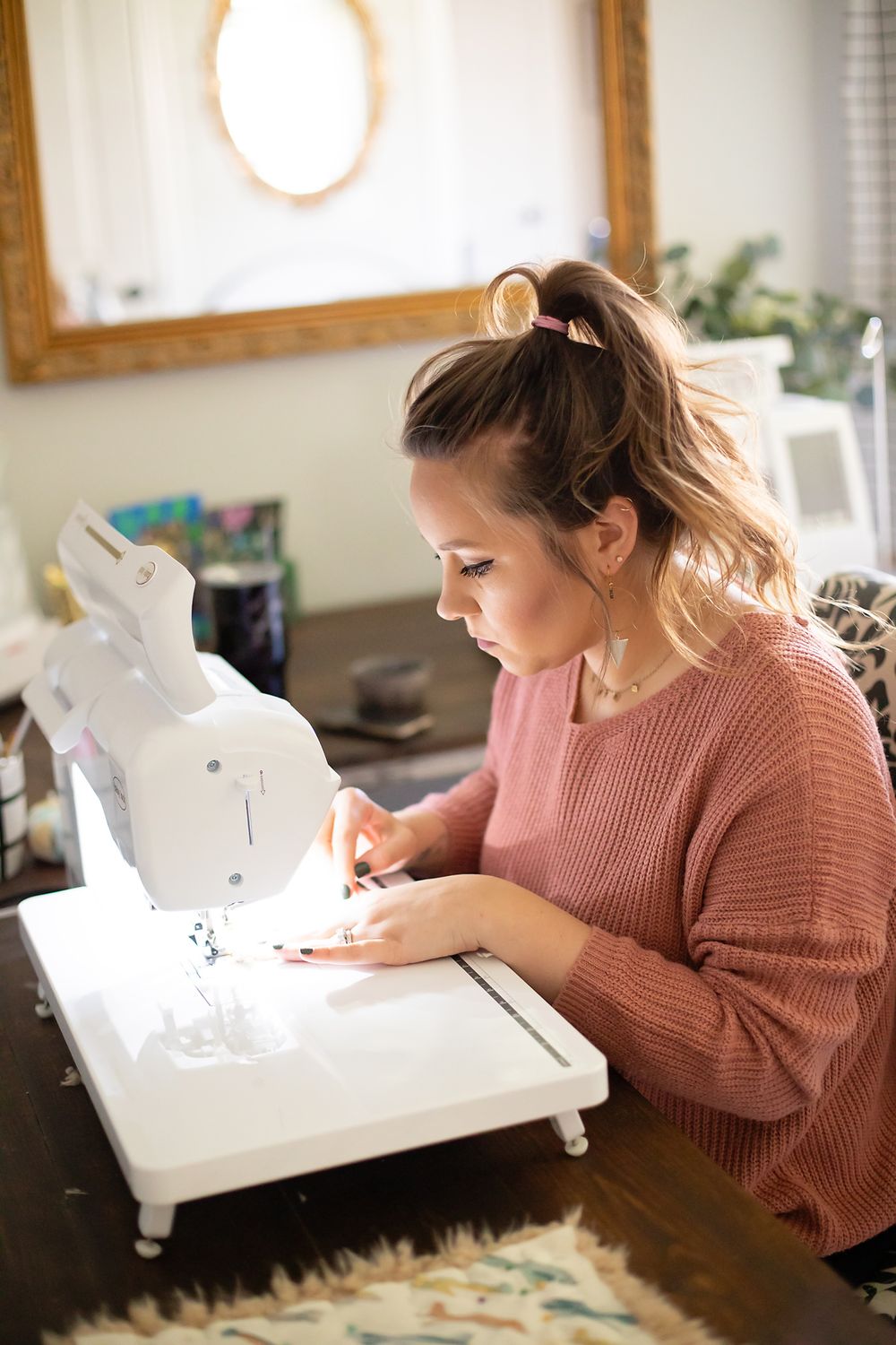 A seamstress in a pink sweater concentrating while working at a white sewing machine.