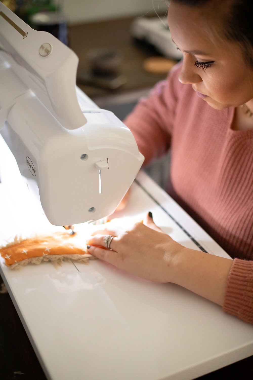 Detailed view of hands guiding fabric through a white sewing machine.