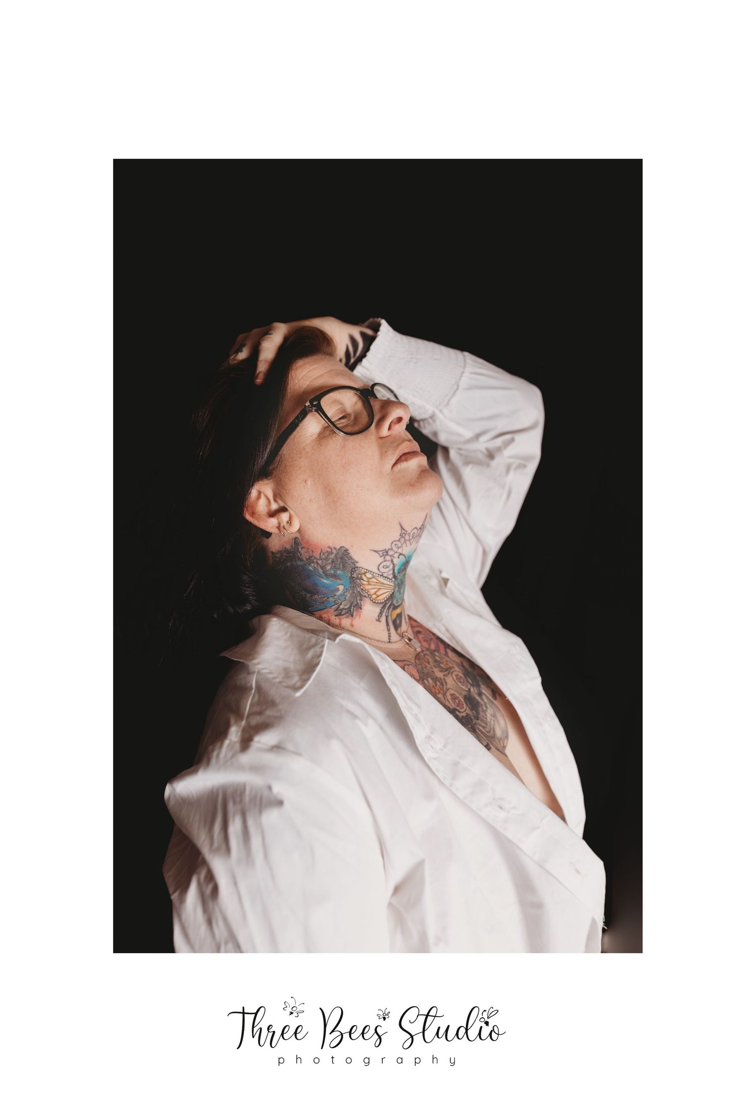 Artistic portrait showing neck tattoos and a white collared shirt against a dark background.