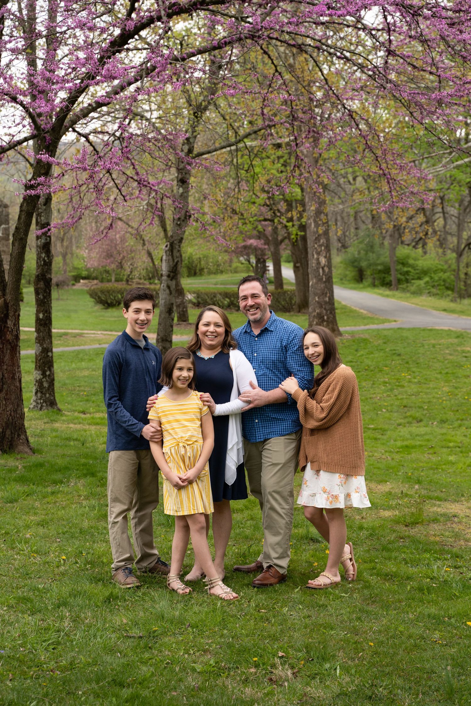 Group portrait under blooming pink cherry blossom trees in a spring park setting.
