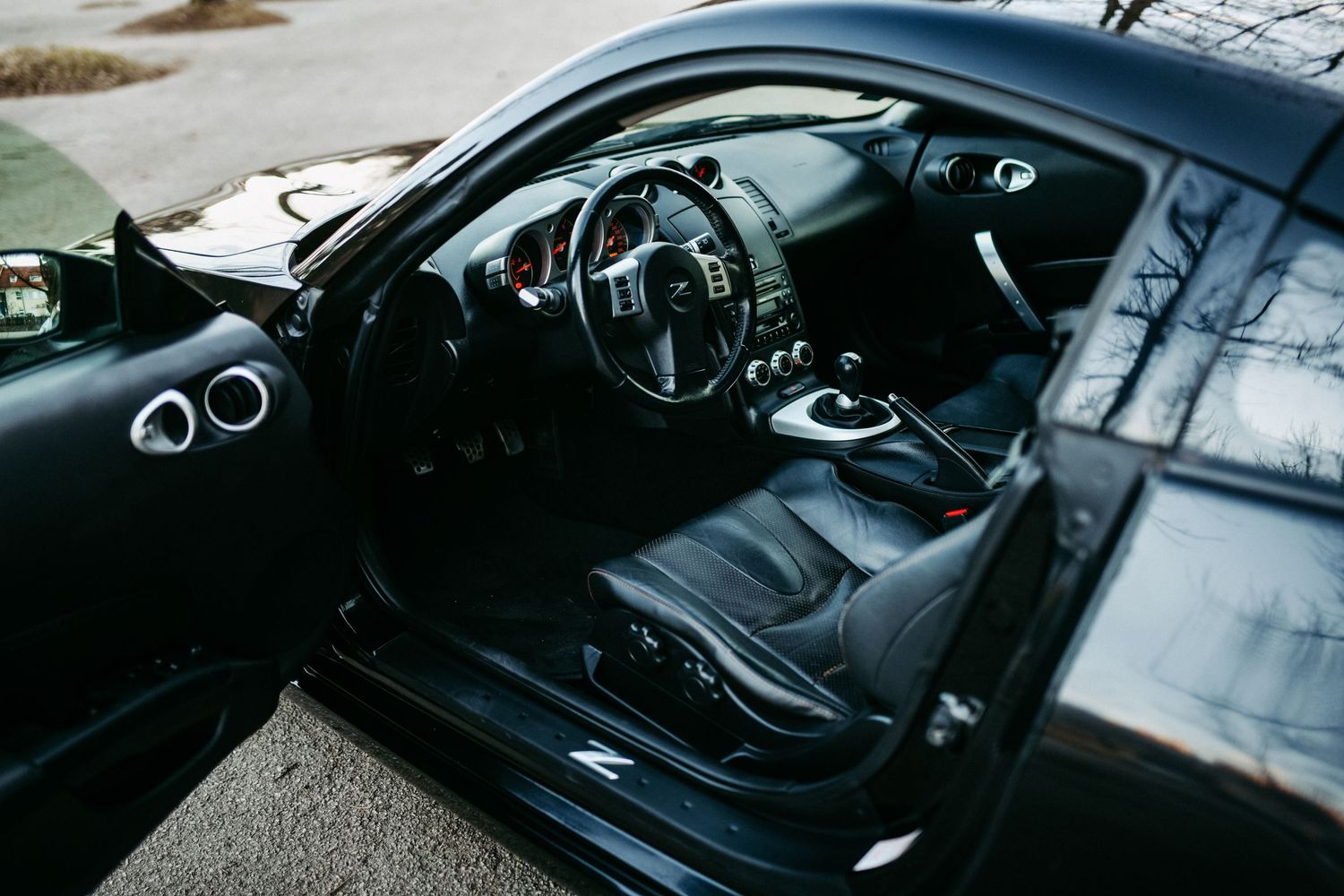 Black leather interior of sports car with door open showing dashboard and seats.