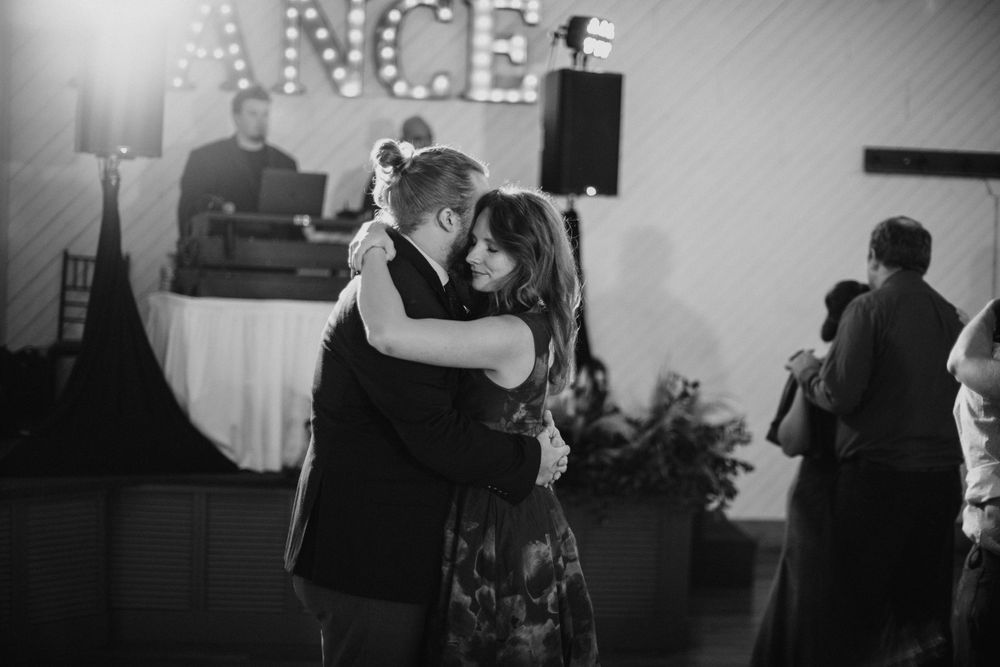 Black and white photo of couple sharing a romantic slow dance at a wedding reception under dim lighting.