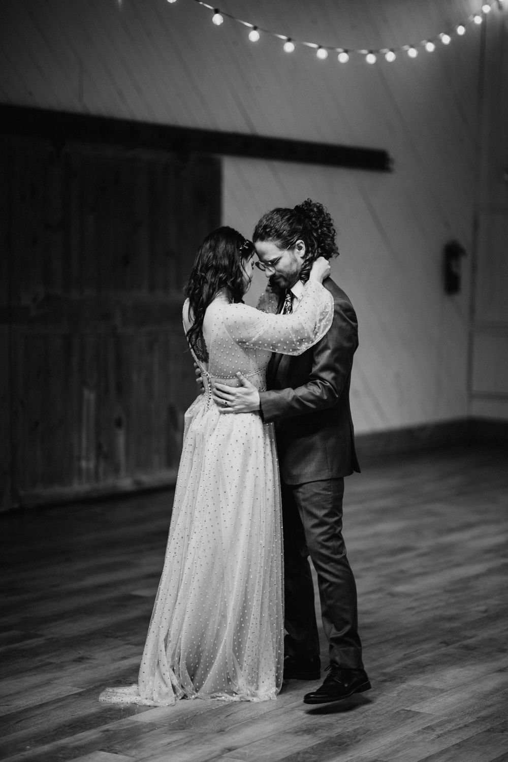 Black and white photo of bride and groom sharing an intimate kiss during their first dance at barn wedding.
