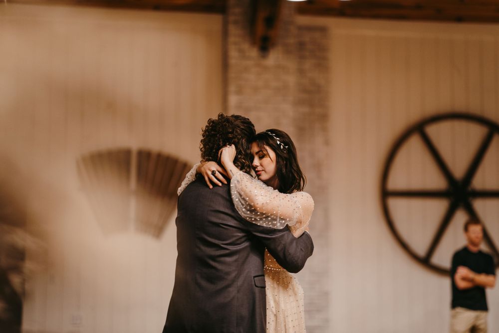 Bride and groom share an emotional embrace during their first dance at a rustic barn wedding reception.