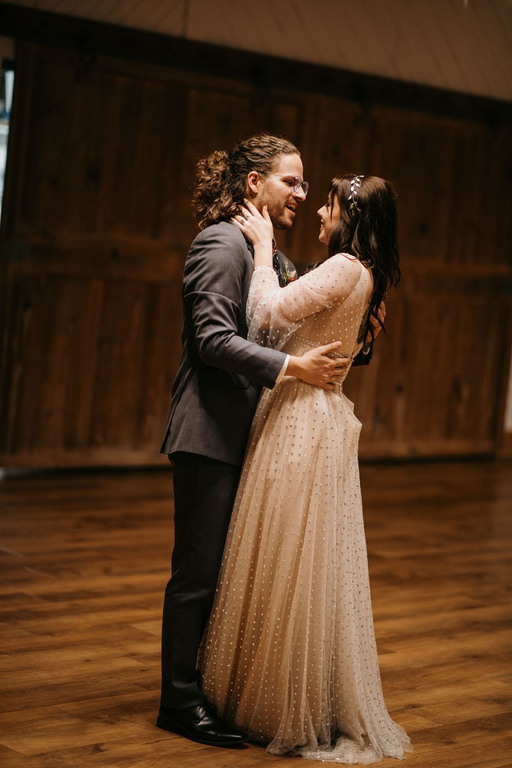Smiling bride and groom gaze lovingly at each other during their first dance in a rustic barn venue.