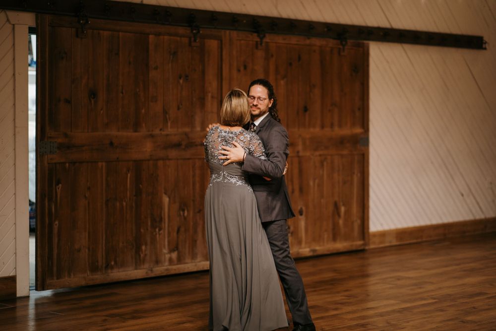 Couple shares a tender embrace on the dance floor in front of rustic wooden barn doors at a wedding reception.