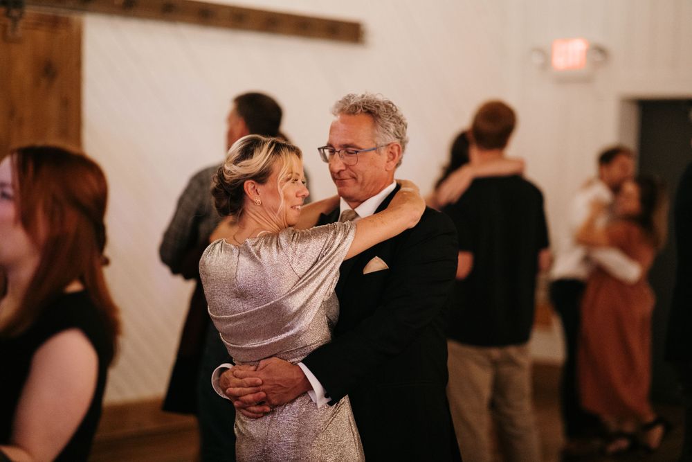 Wedding guests share a romantic slow dance together in a bright white barn reception venue.